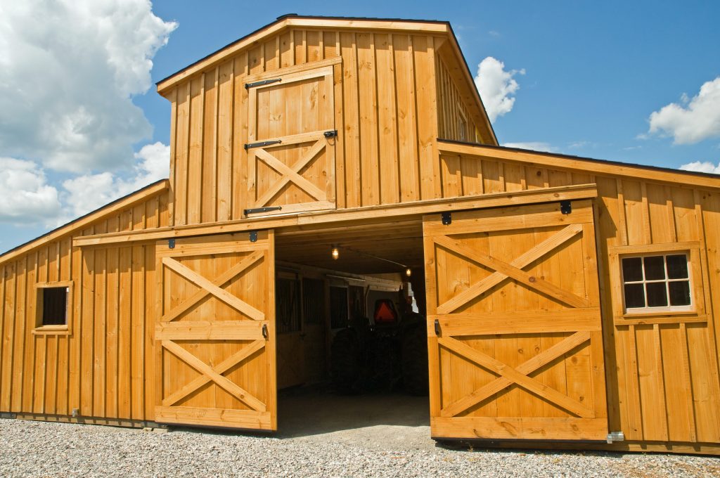 A view of a new wooden farm barn with sliding doors and a second story.