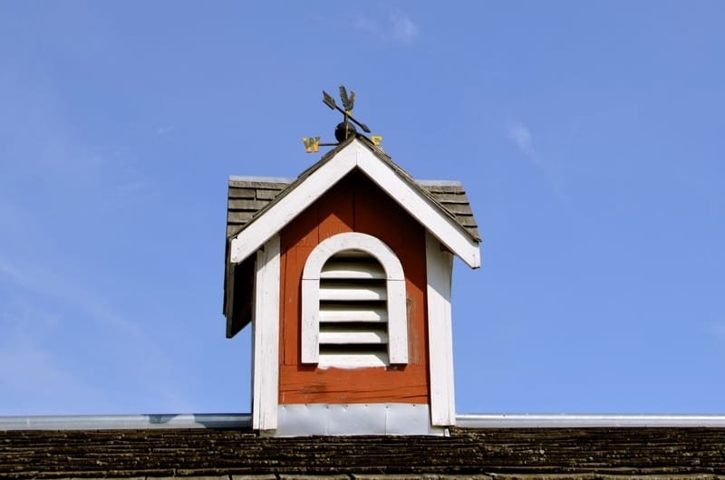 The roofline of a barn displays a wooden cupola with a wind vane.